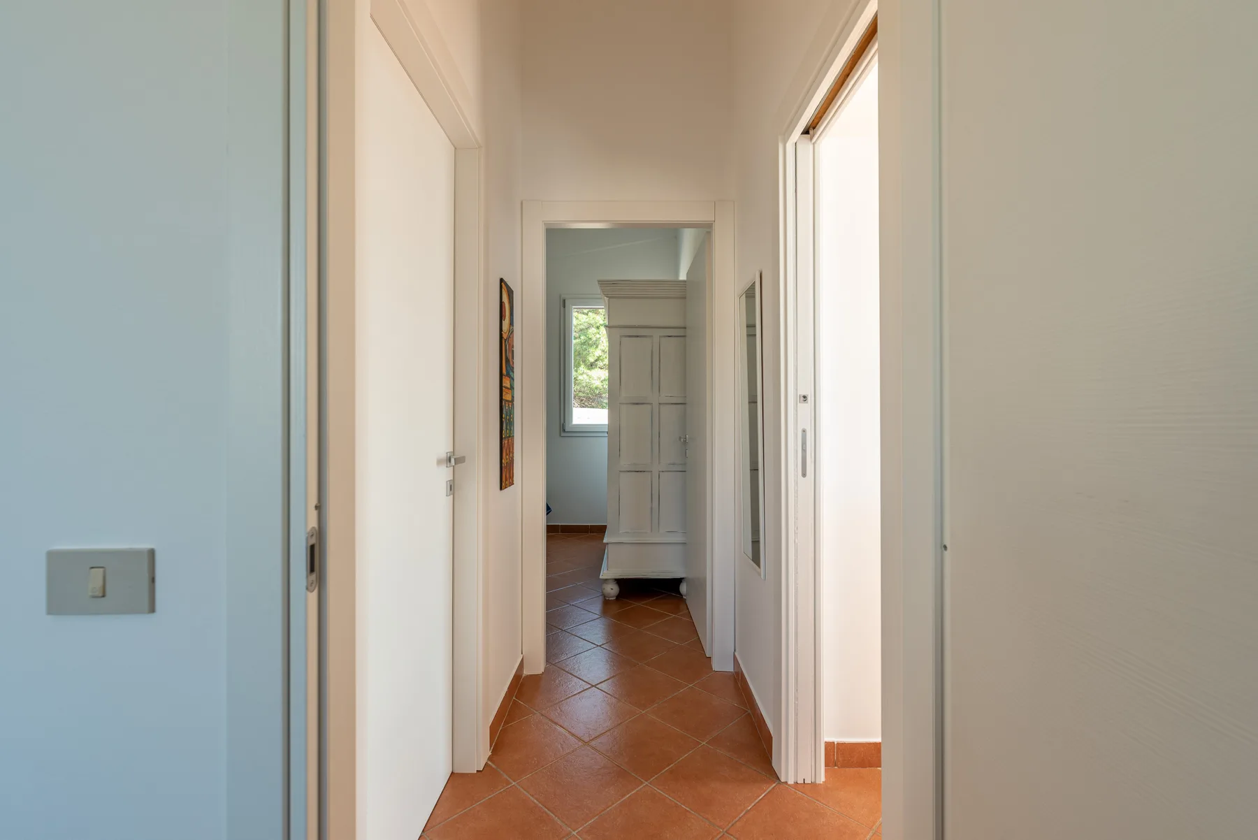 Un pasillo luminoso con suelo de baldosas color terracota y varias puertas.