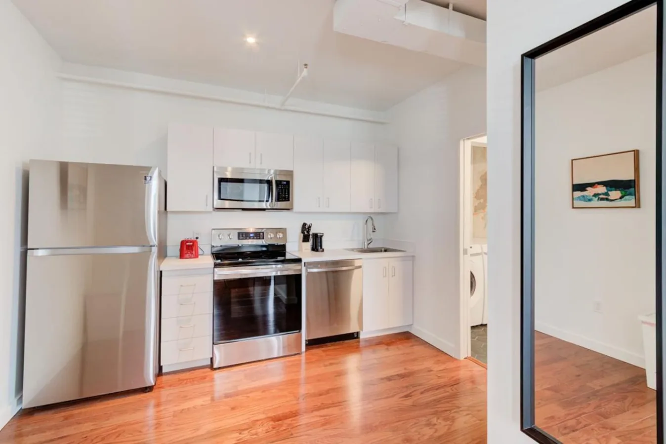 Una cocina luminosa con gabinetes blancos, electrodomésticos de acero inoxidable y piso de madera.