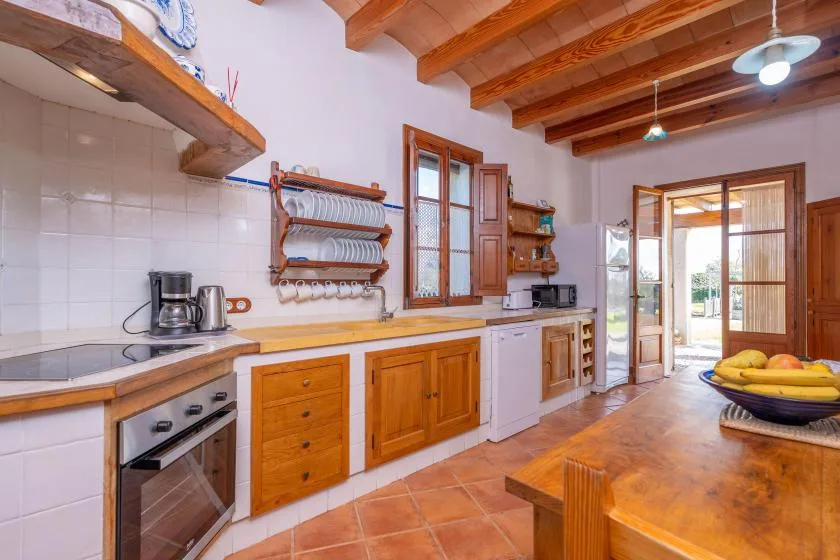 Una cocina con gabinetes de madera, encimeras de azulejos y una puerta abierta al patio.