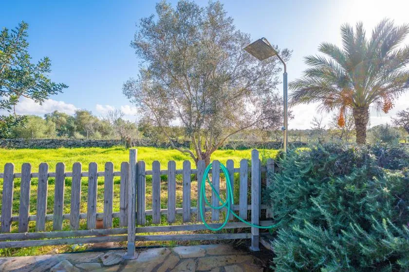 Un jardín vallado bordea un campo verde, con árboles y arbustos cerca.