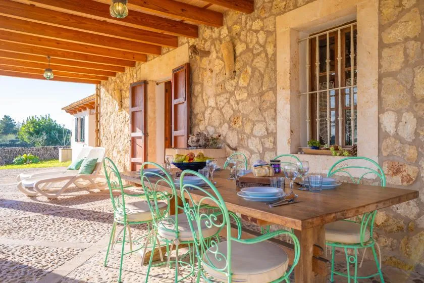 Un patio cubierto de piedra con una mesa de comedor de madera y sillas verdes.