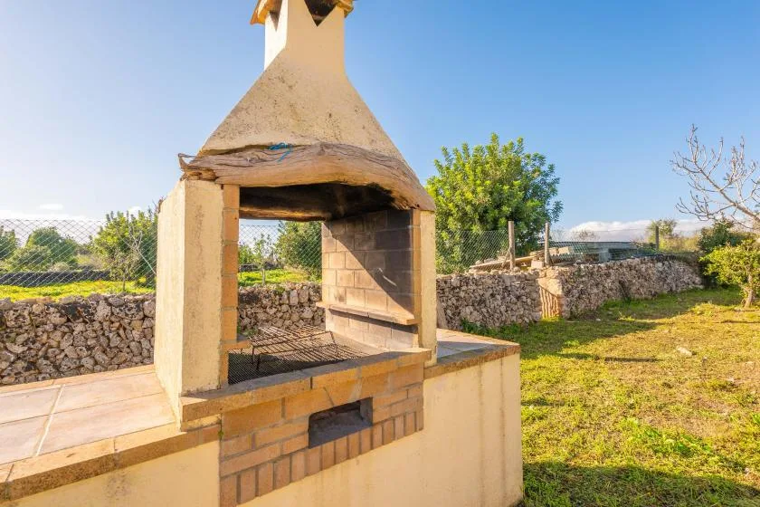 Una barbacoa de obra al aire libre está junto a un muro de piedra en un patio con césped.