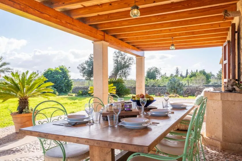 Comedor exterior cubierto con una mesa puesta frente a un jardín.