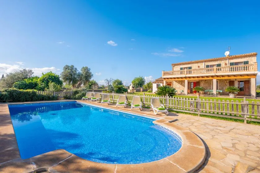 Una piscina al aire libre junto a una casa de dos plantas y un patio.