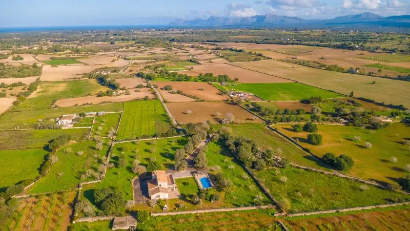 Vista aérea de campos agrícolas en mosaico, con una casa y una piscina en primer plano.
