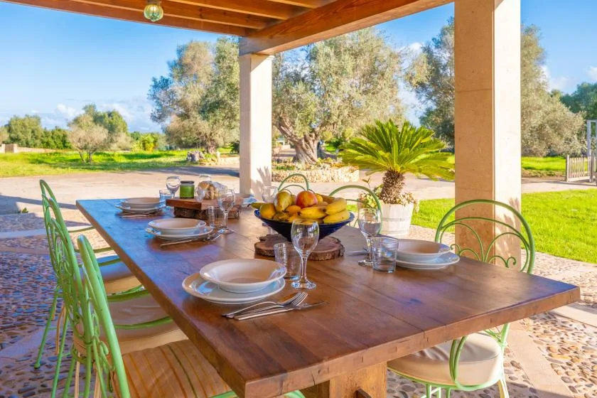 Una zona de comedor exterior cubierta tiene una mesa de madera puesta con platos y fruta.