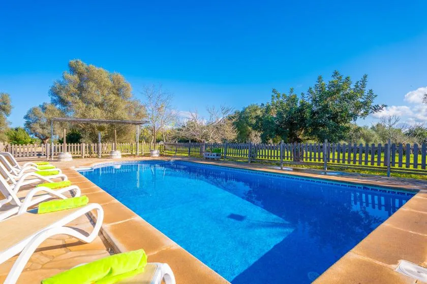 Una piscina al aire libre está rodeada de tumbonas y un patio cercado.