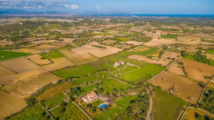 Vista aérea de campos de cultivo variados, casas dispersas y la costa a lo lejos.