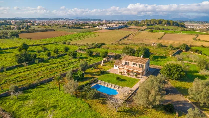 Una casa en el campo está rodeada de campos verdes, con una piscina a su lado.