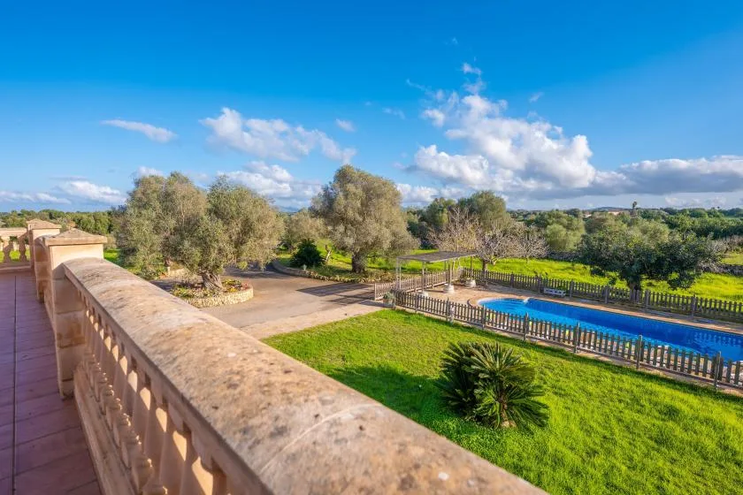 Una terraza da a una piscina y a unos jardines verdes.