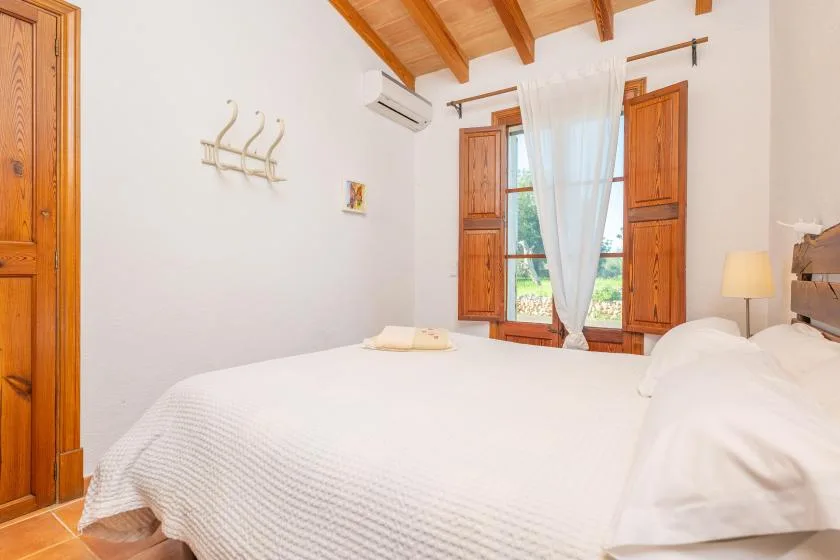 Un dormitorio luminoso con una cama blanca y contraventanas de madera alrededor de la ventana.
