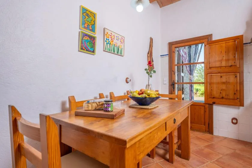 Una mesa de comedor de madera está en una habitación luminosa junto a una ventana abierta.