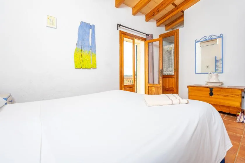 Un dormitorio con una cama bien tendida, vigas de madera en el techo y una puerta abierta.