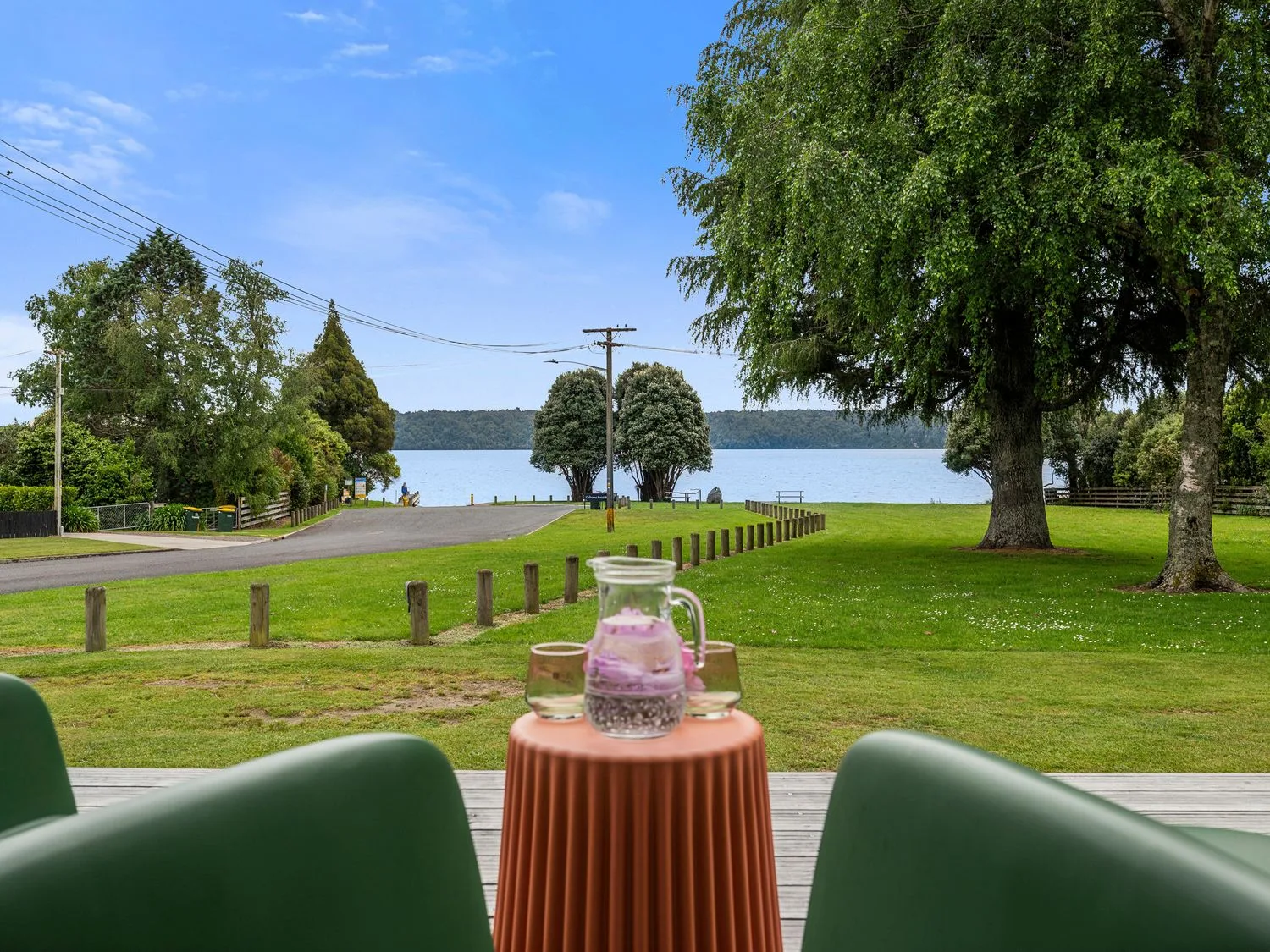 A lakeside lawn with trees and a paved road beside the water.