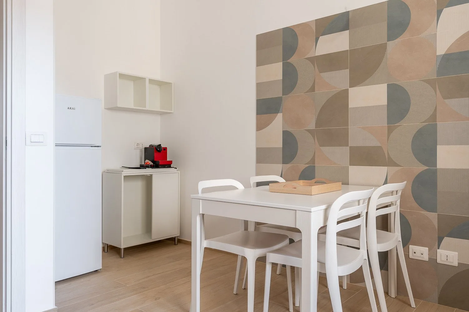Comedor con una mesa blanca y sillas junto a una pequeña zona de cocina.