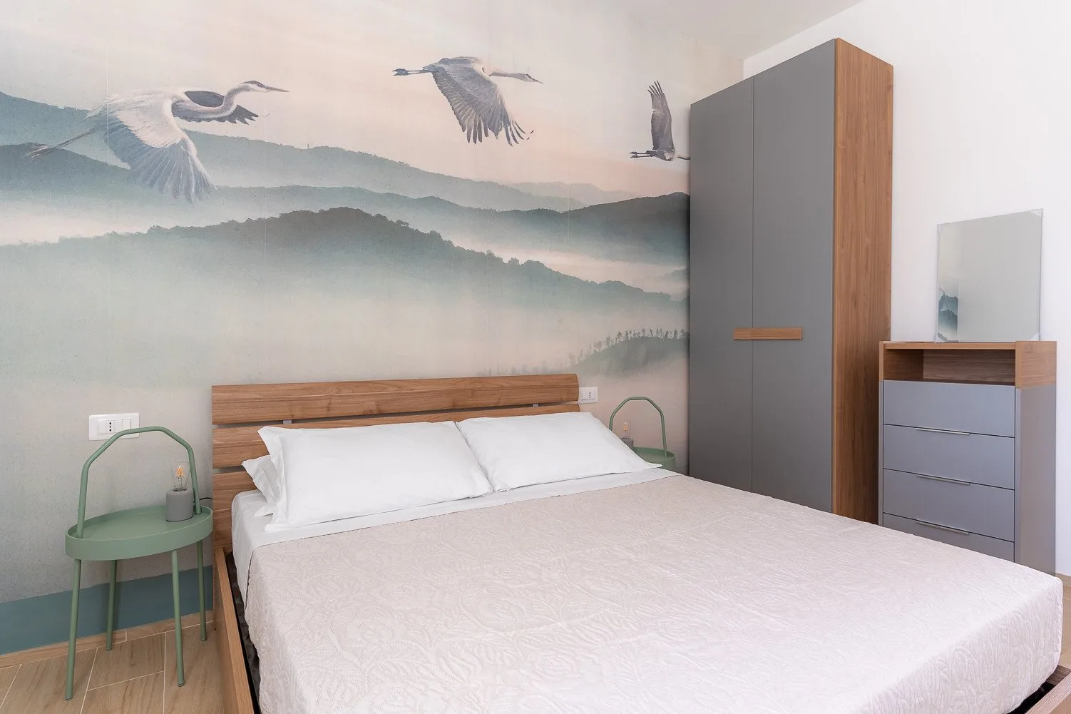 Un dormitorio con una cama grande y un mural de aves sobre colinas brumosas.