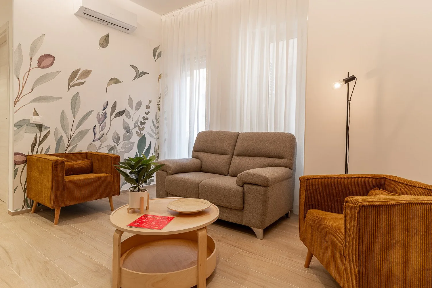 Una sala de estar con asientos, una mesa de centro y un mural de hojas.