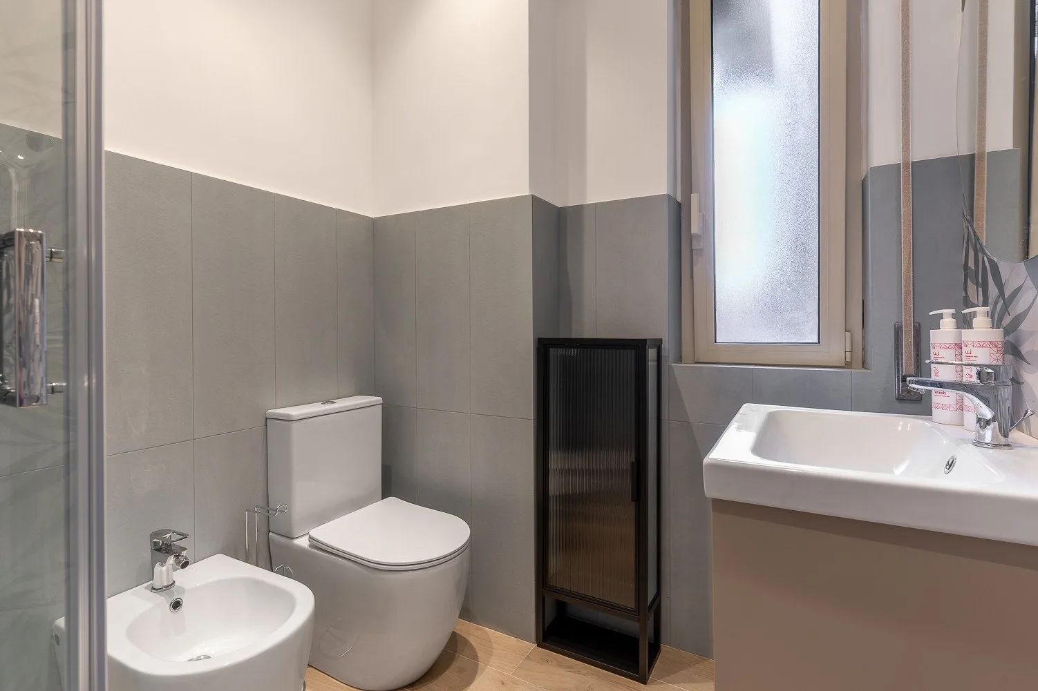 Un baño con inodoro, bidé y lavabo junto a una ventana esmerilada.