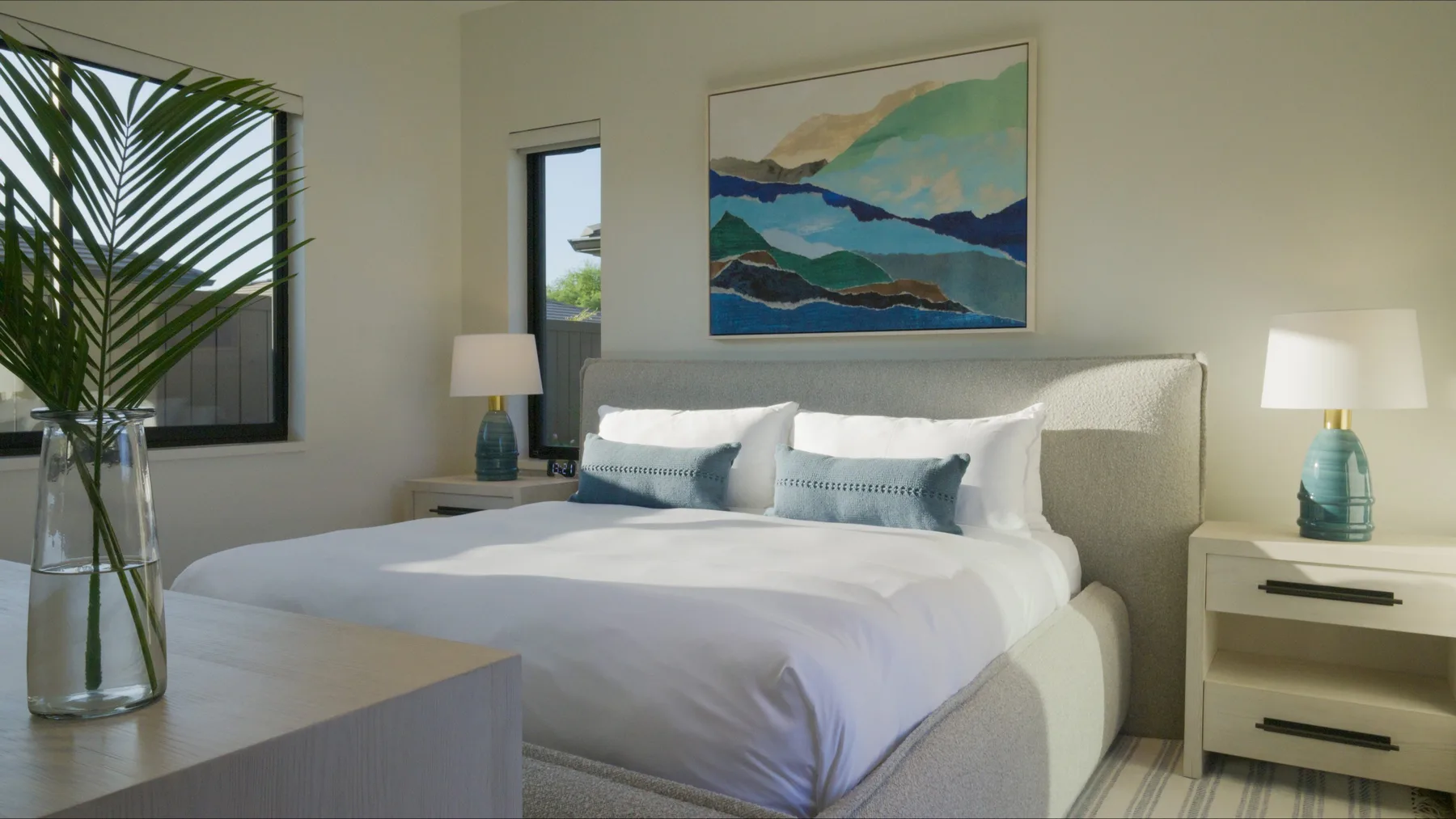 Un dormitorio con una cama bien hecha, mesitas de noche y una colorida obra de paisaje.