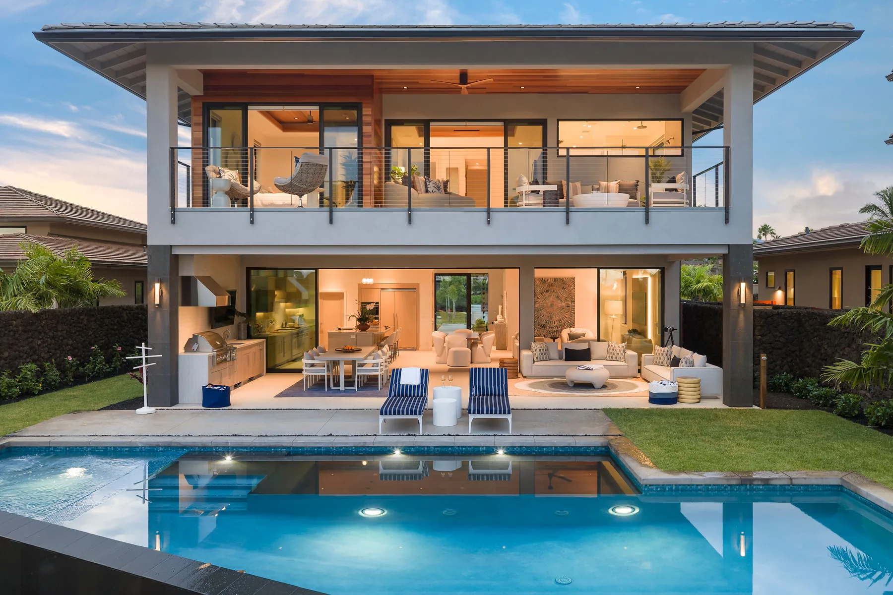 Una casa moderna de dos plantas da a una piscina, con balcones y zonas de patio amuebladas.