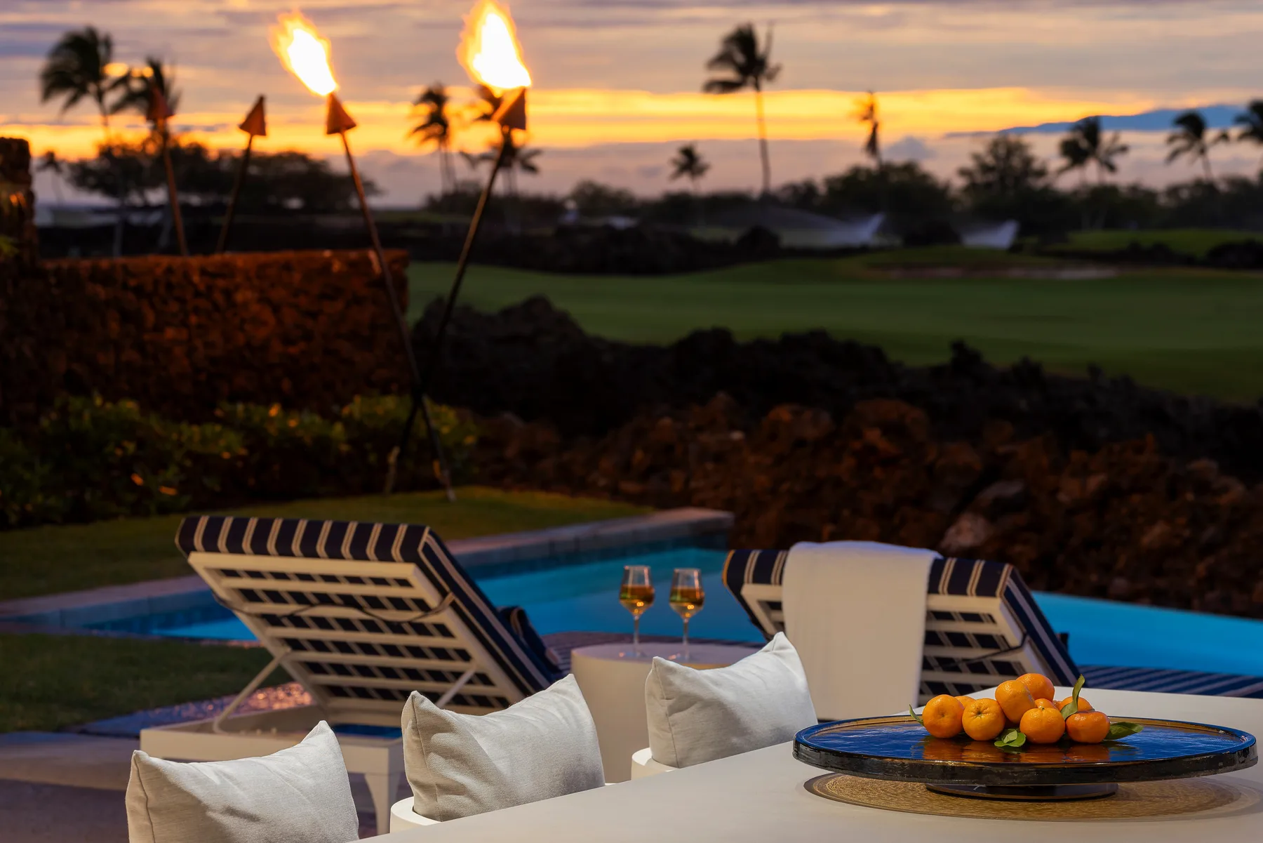 Una zona de estar junto a la piscina tiene vistas a un campo de golf al atardecer.