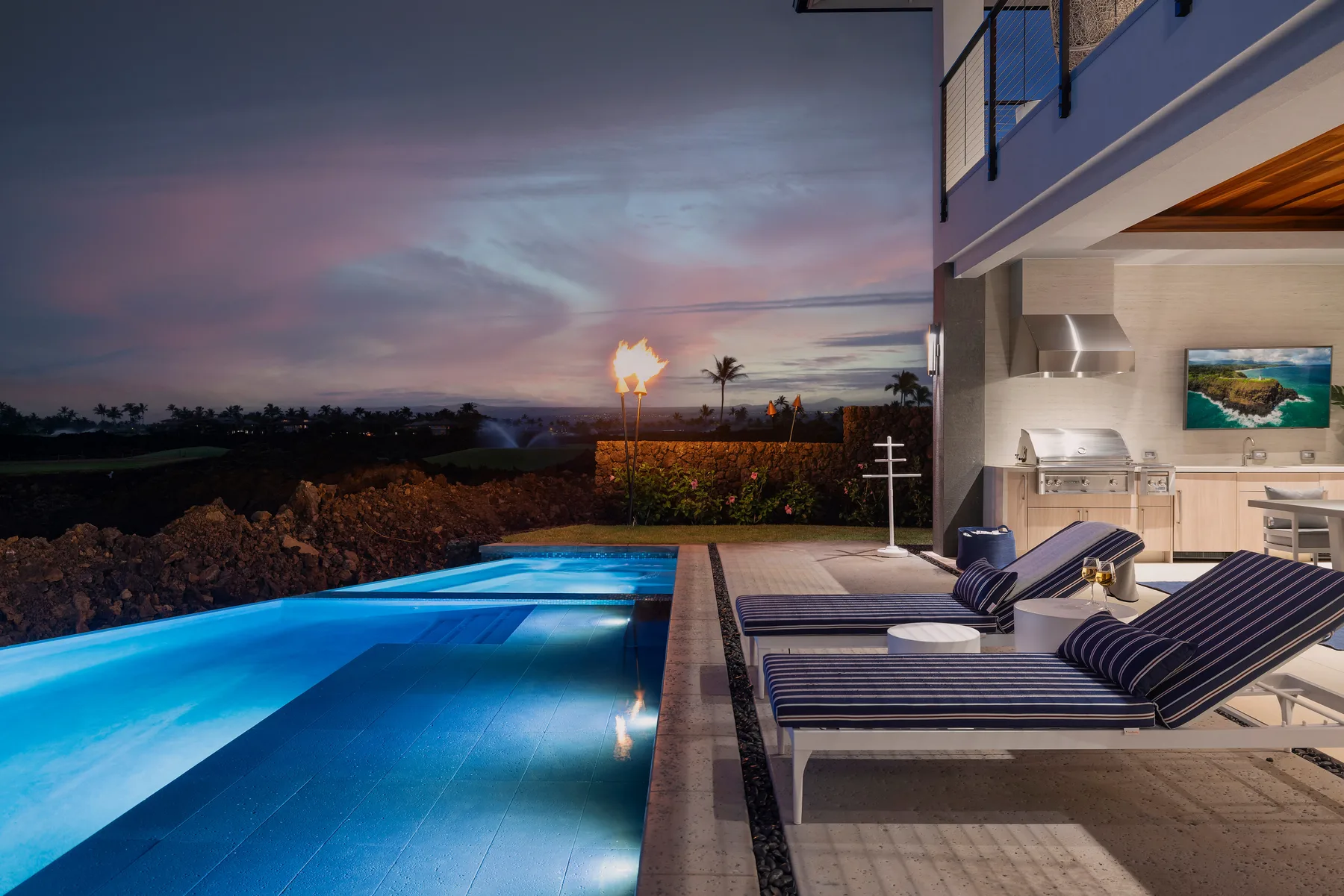 Una piscina exterior junto a un patio moderno con asientos reclinables al anochecer.
