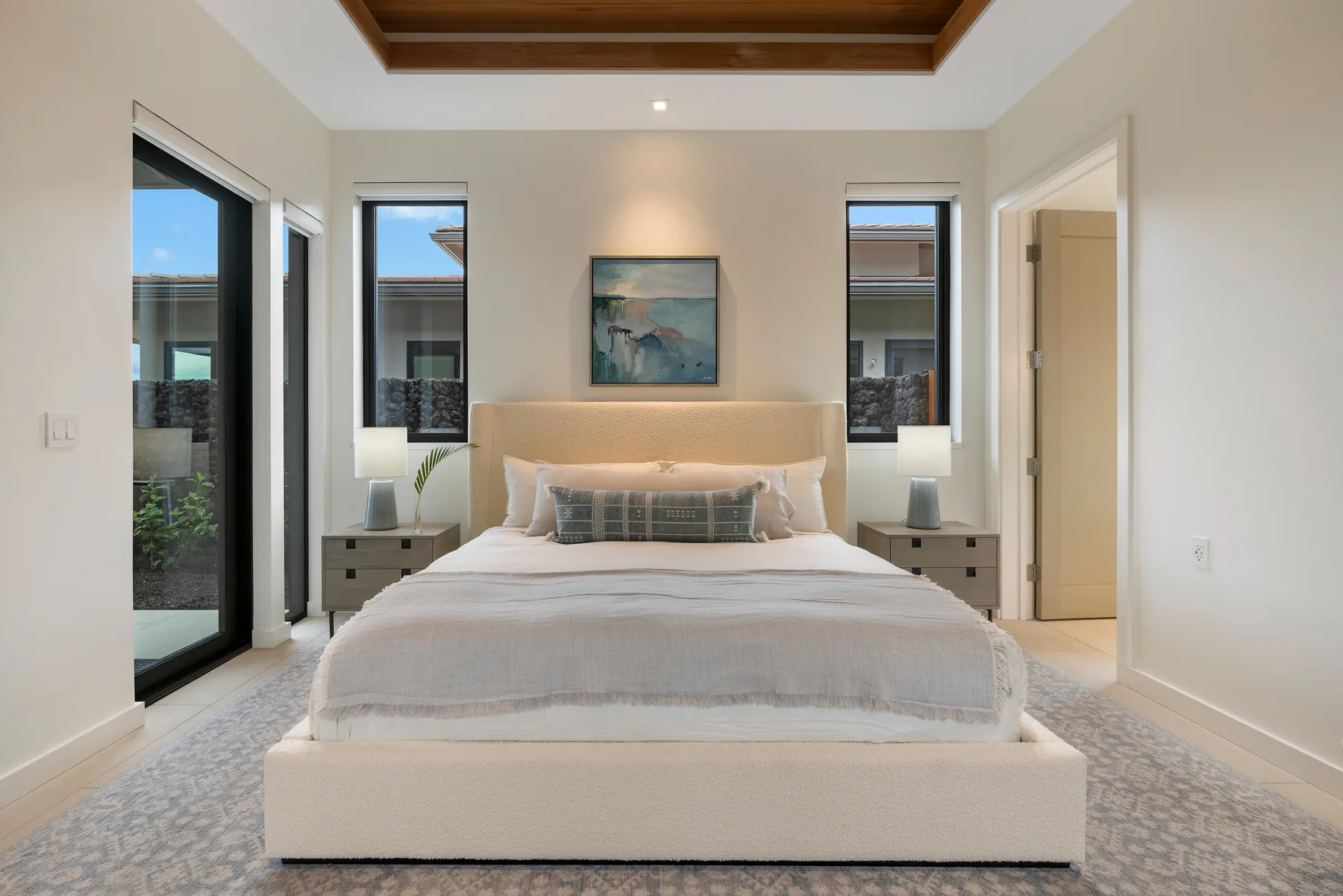 Un dormitorio luminoso con una cama grande, mesitas de noche y ventanas altas.