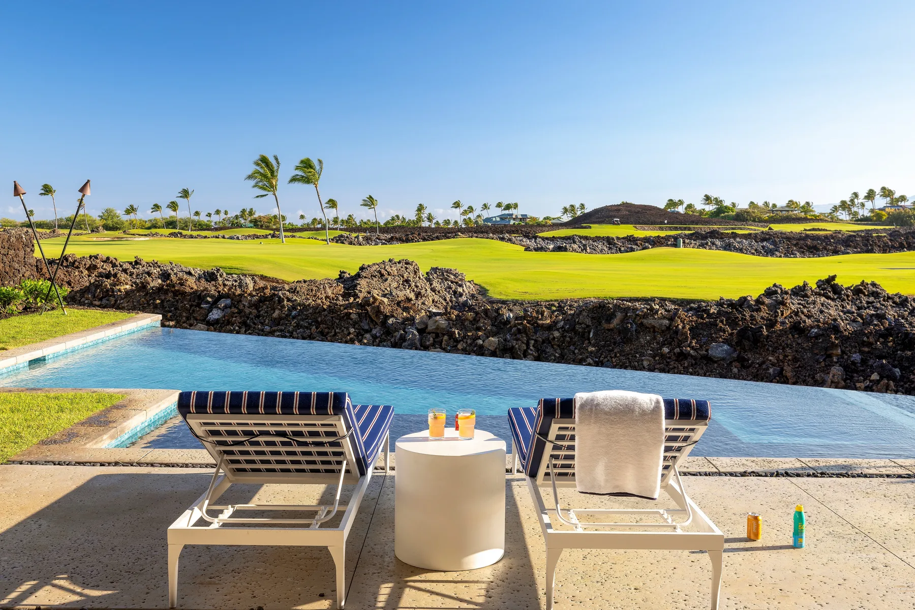 A poolside patio overlooks a green golf course, with lounge seating beside the water.