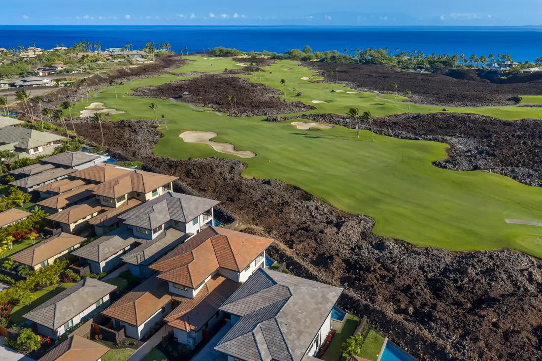 Vista aérea de un campo de golf junto a viviendas, con el océano al fondo.