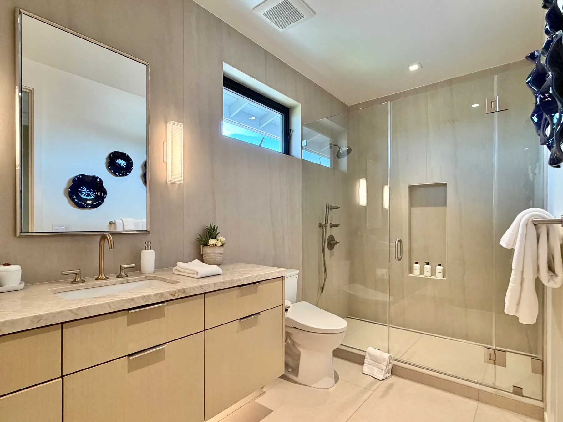 Un baño luminoso con un tocador largo, espejo, inodoro y ducha de vidrio.