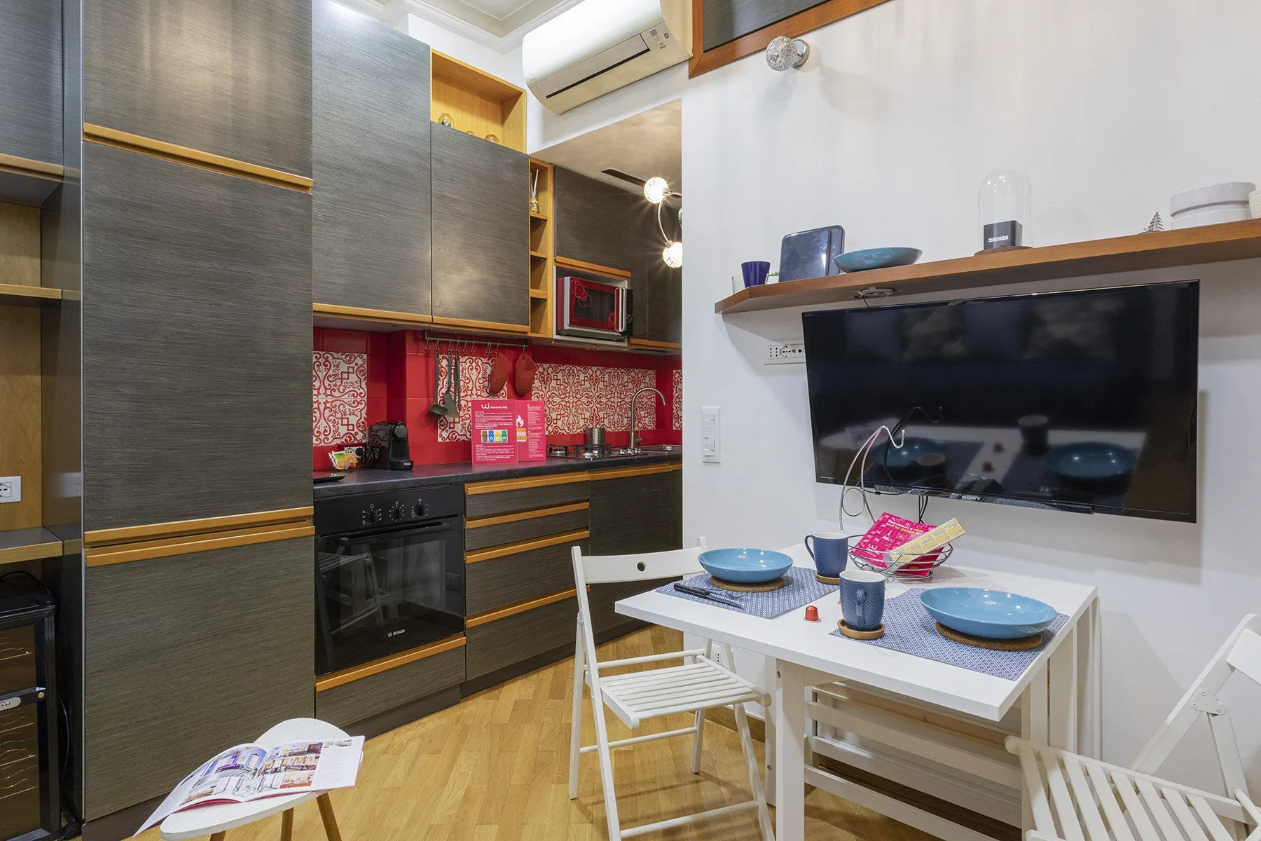Una cocina compacta con gabinetes oscuros, una placa de cocina y una mesa puesta con platos.