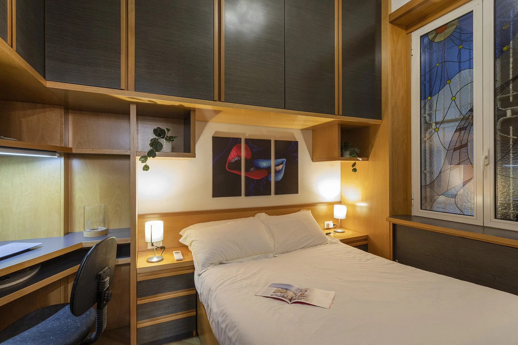 Un dormitorio con una cama tendida bajo armarios superiores oscuros.