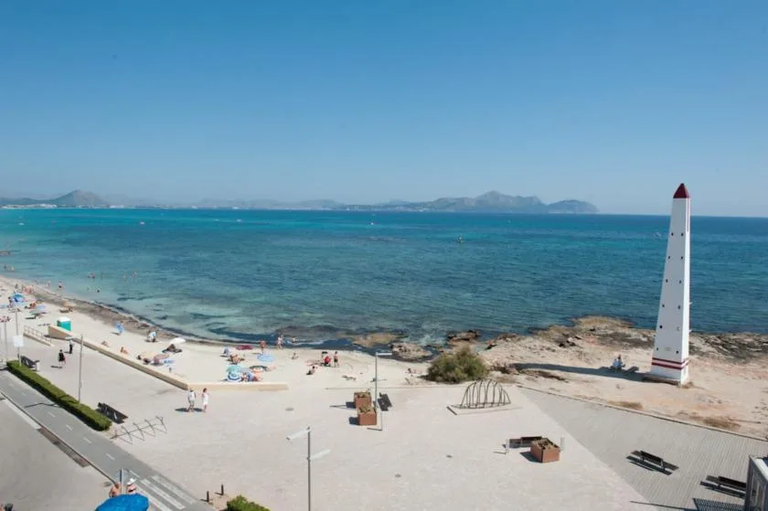 A seaside beach and promenade overlook turquoise water and distant mountains.
