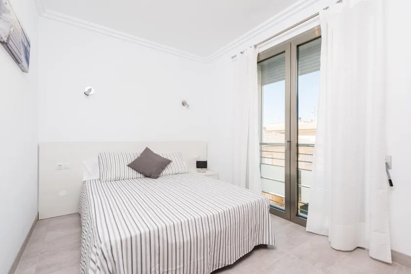 A bright bedroom with a striped bed and glass doors opening to a balcony.