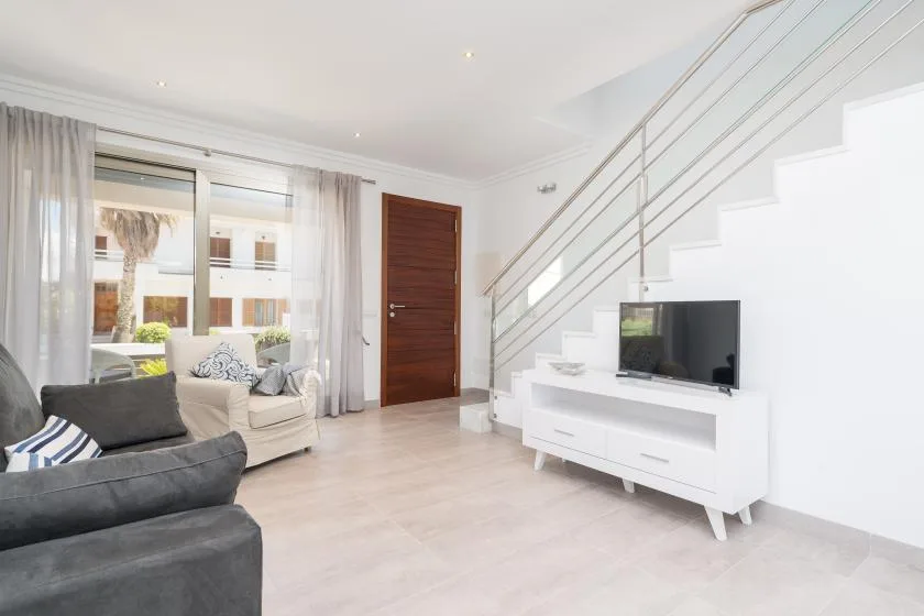 A bright living room with seating, a television, and a staircase.