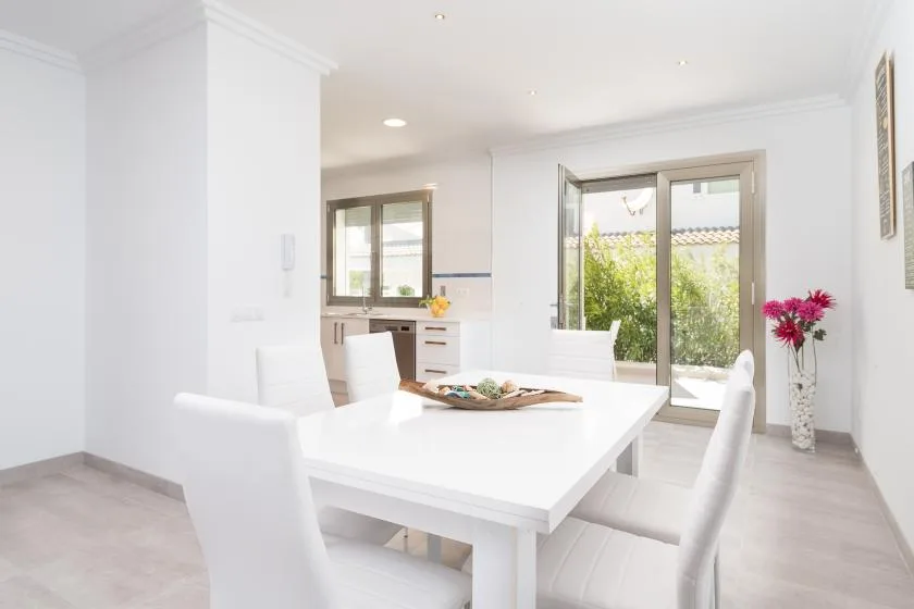 A bright dining area with a white table beside large windows and a sliding glass door.