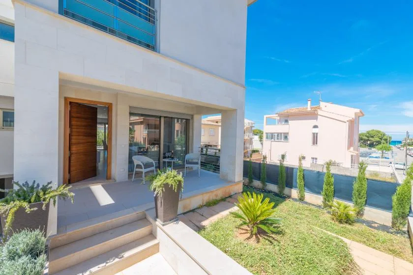 A sunny patio beside a modern white building, with outdoor seating and a small garden.