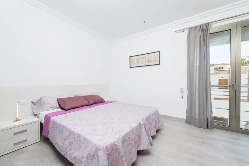 A bright bedroom with a bed beside a curtained glass door.