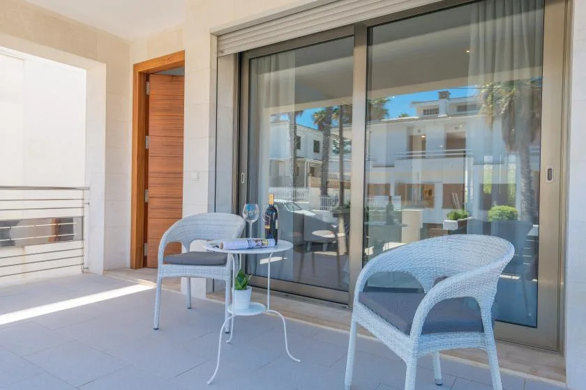 A bright patio with two woven seats and a small round table by sliding glass doors.