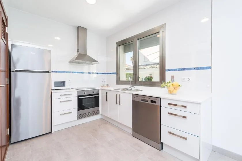 A bright kitchen with white cabinetry, a refrigerator, and a window above the counter.