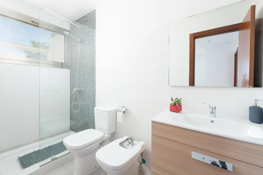A bright bathroom with a glass shower, toilet, and wood-toned vanity.