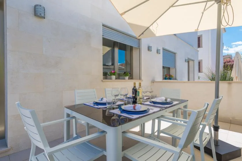 A terrace dining area with a set table beneath a large umbrella.