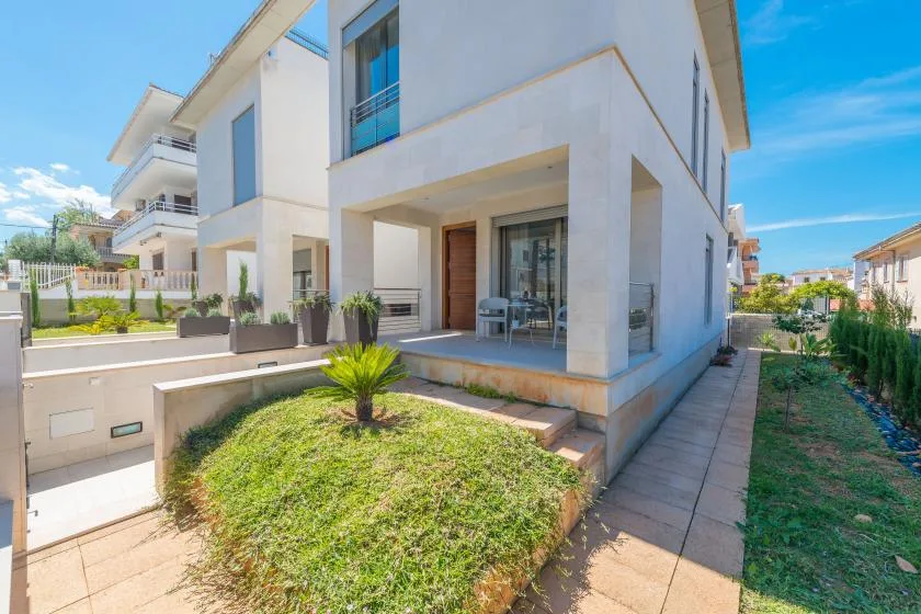 A modern house with a covered patio beside a small lawn and paved walkway.