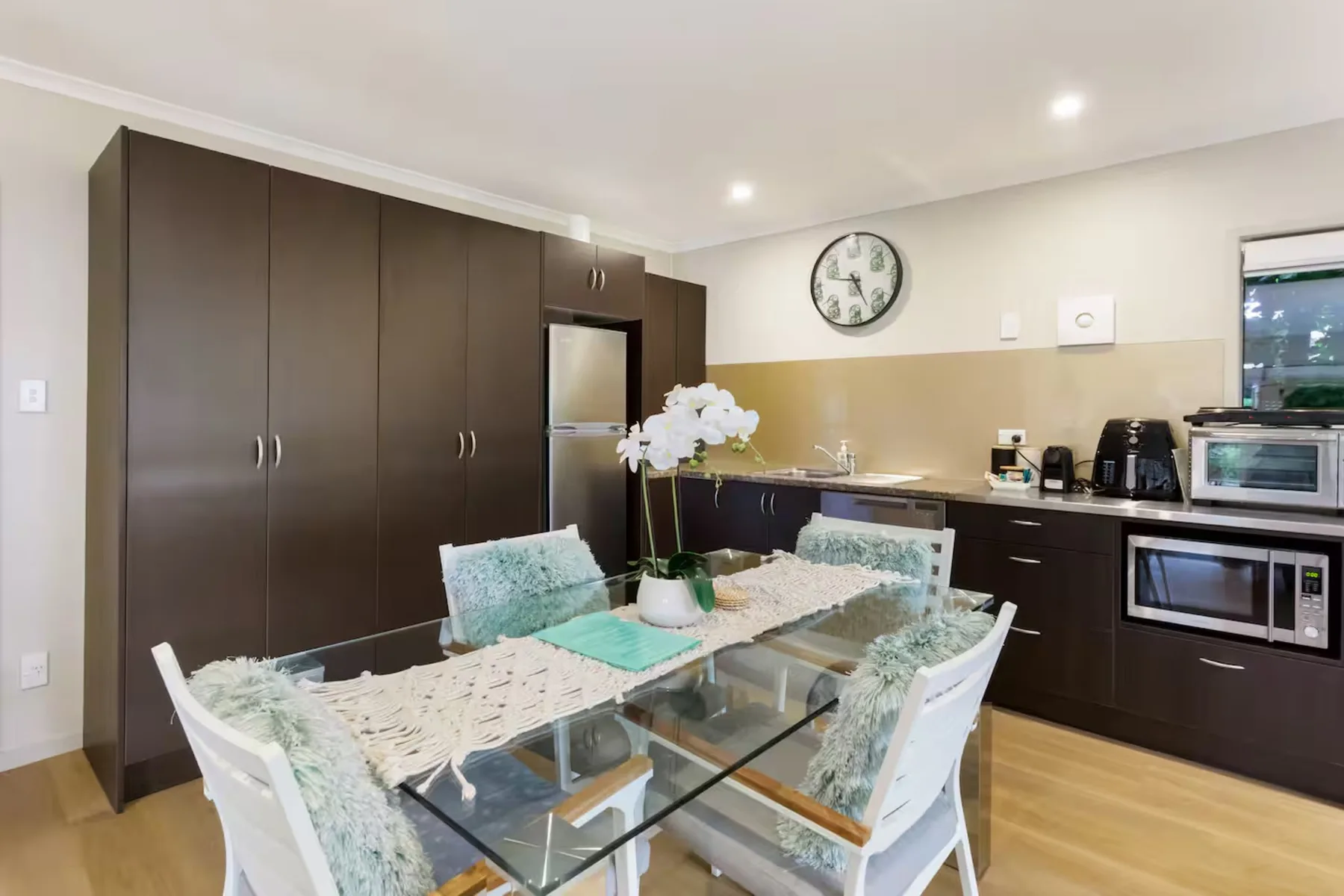 A dining area with glass-top seating beside dark kitchen cabinets.