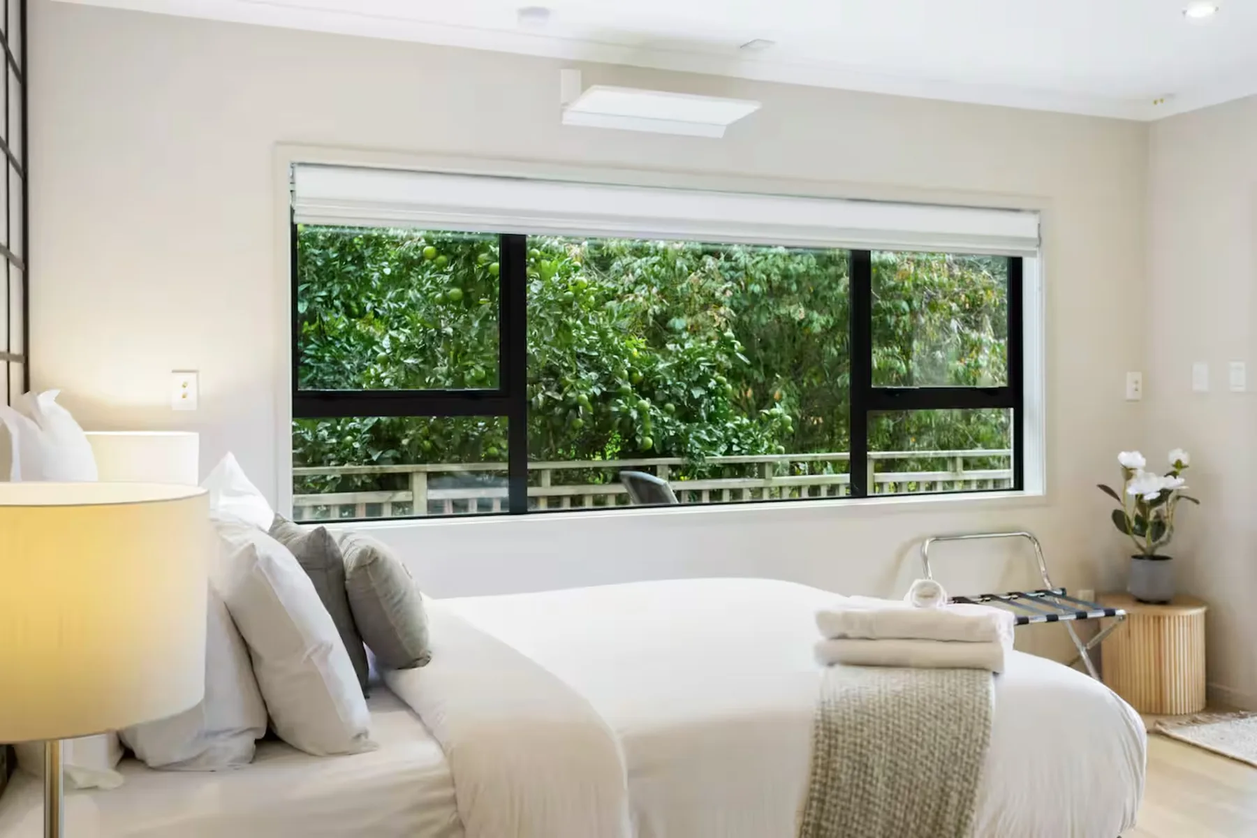 A bright bedroom with a large window overlooking leafy greenery.