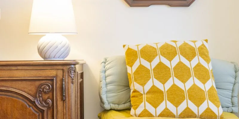 Una zona de asientos con cojines claros y un cojín amarillo estampado junto a una mesa de madera.