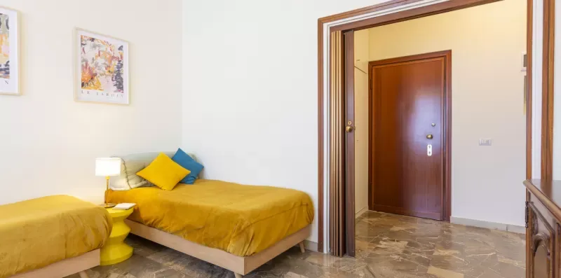 Un dormitorio con una cama vestida de amarillo y almohadas azules junto a una mesita.