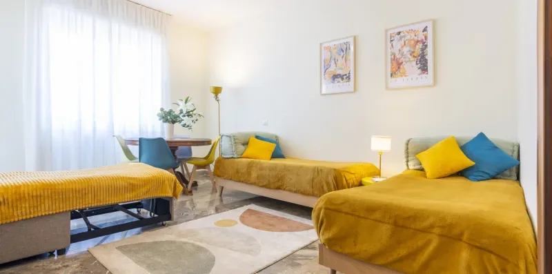 Un dormitorio con camas color mostaza, cojines de colores y una alfombra.