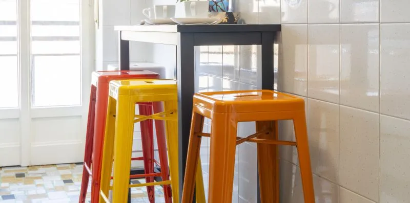 Una cocina luminosa con taburetes de colores junto a una ventana grande.