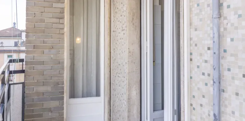 Una puerta de balcón con paredes de azulejos claros y una cortina.